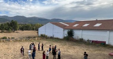 Rappresentazione di una scuola in un'area rurale, con persone in cerchio intente in qualche tipo di attività.