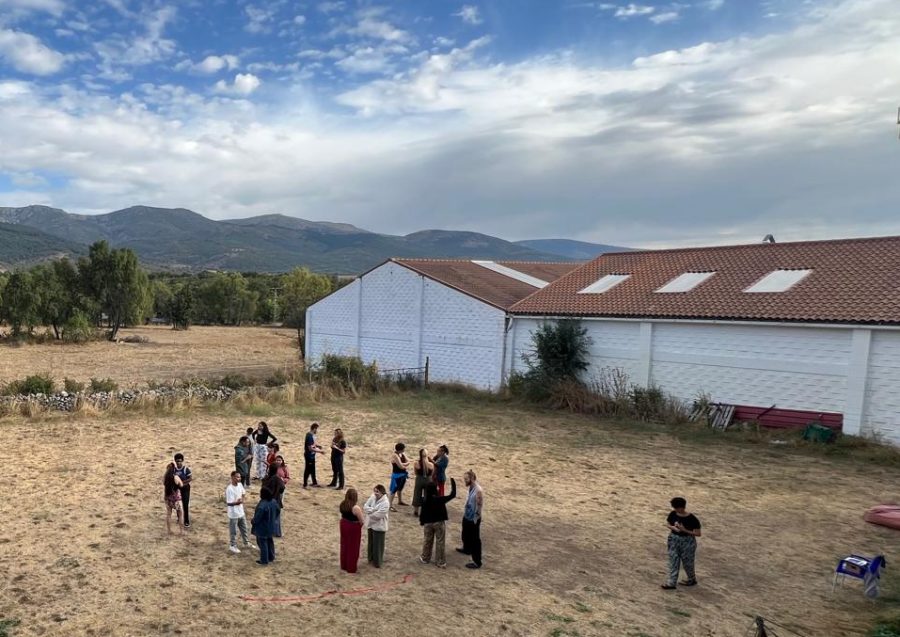 Rappresentazione di una scuola in un'area rurale, con persone in cerchio intente in qualche tipo di attività.