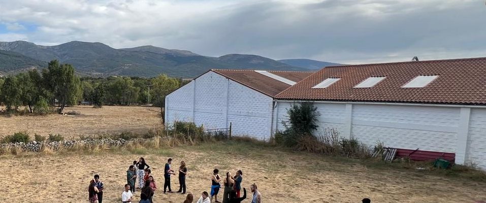 Rappresentazione di una scuola in un'area rurale, con persone in cerchio intente in qualche tipo di attività.